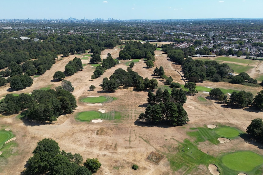 An aerial view of a dry golf course with a large city skyline in the background.
