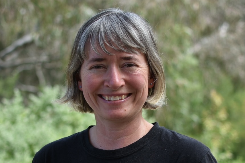 A woman with gray hair and brown eyes smiles at the camera.