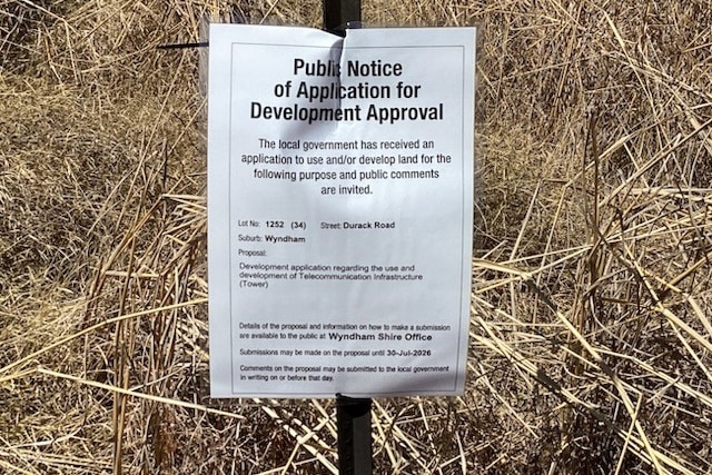 A small sign on a stick surrounded by grass