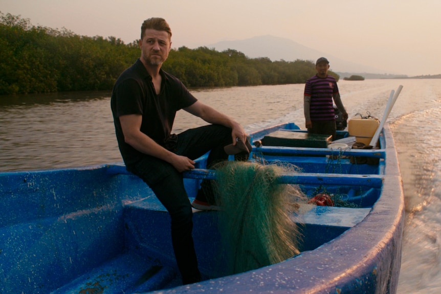 Ben McKenzie on a wooden boat with a local steering.