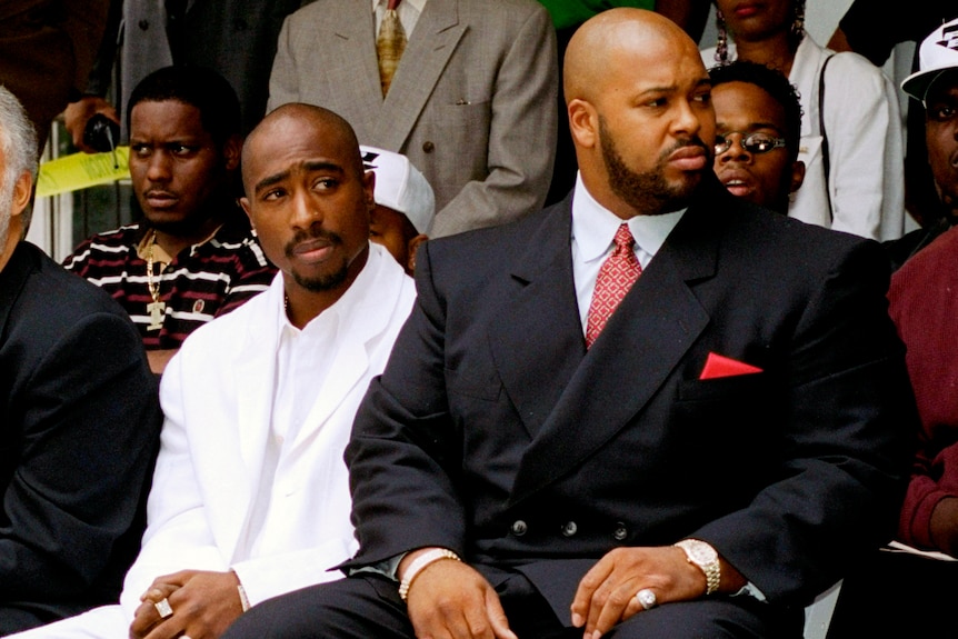 Tupac Shakur and Shuge Knight sit on two chairs in front of a crowd