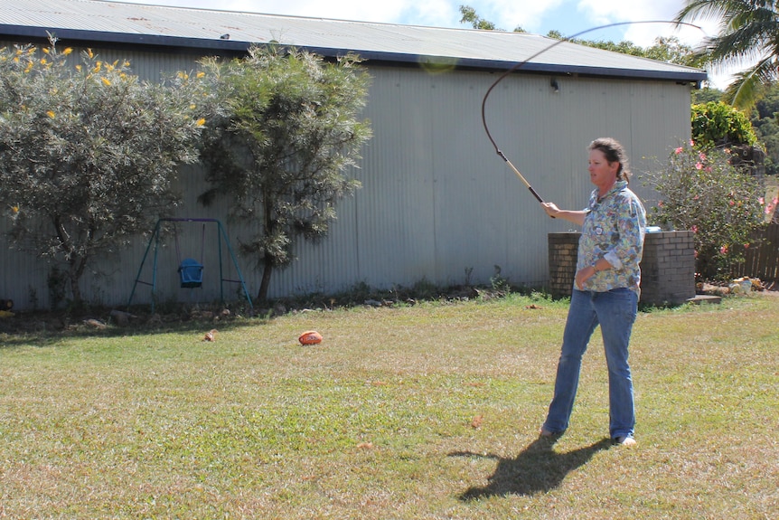 A woman swings a stockwhip high in the air ready to crack it.