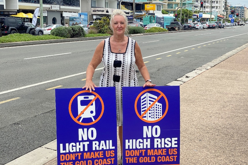 Woman with hair pulled back in ponytail stands on side of road with two signs with crosses through a tall building and phone.