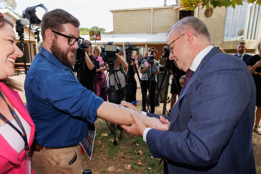 Anthony Albanese smiles as he signs ‘No Change To WA GST’ on a reporter's arm.