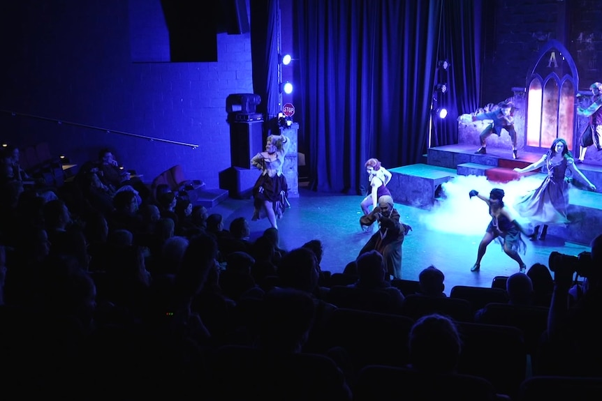A view from above showing people performing on a stage under blue lighting.