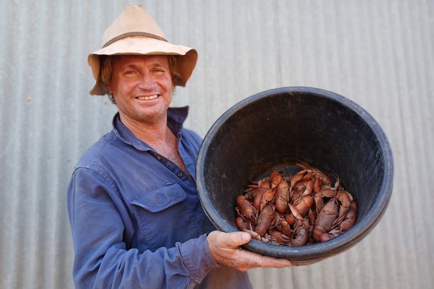 A man holds a bucket filled with yabbies, smiling.