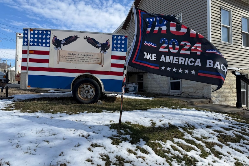 A flag in the snow that says 'Trump 2024: Take America Back'.