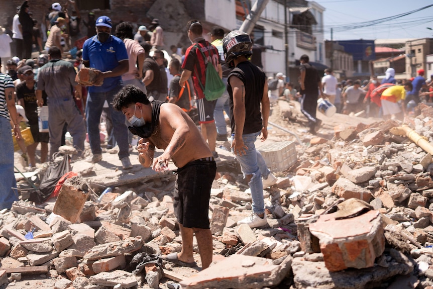 A young man picking through debris strewn on the ground of a city street.