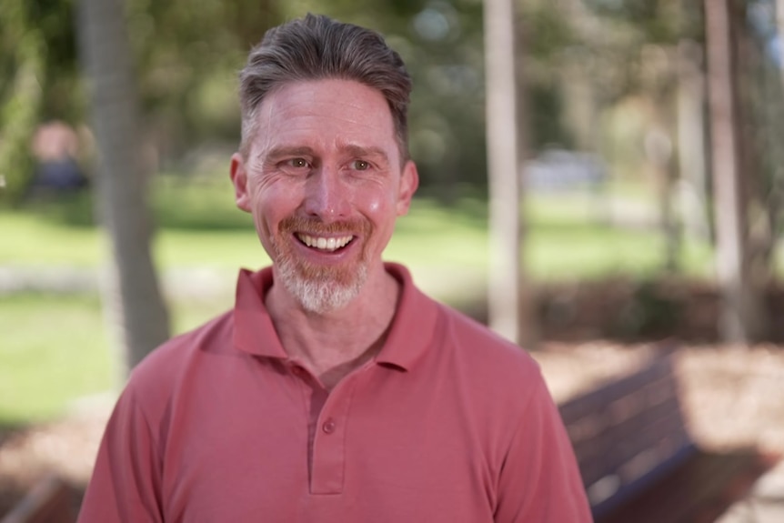 Man in pink shirt smiles in park