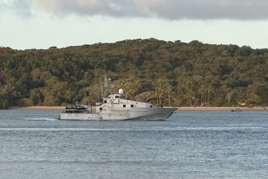 A grey boat on the water near an island.