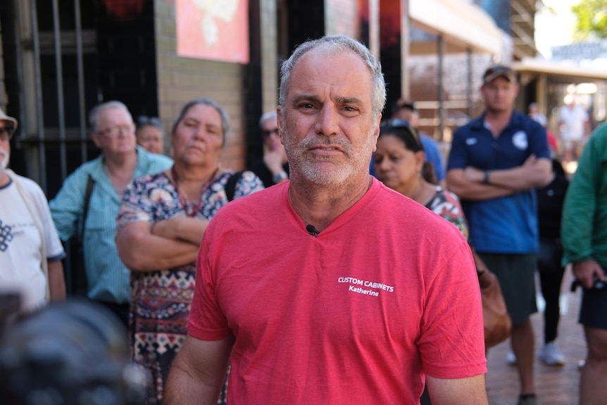 Jeff Usher looks at the camera while a crowd assembled behind him folds their arms.