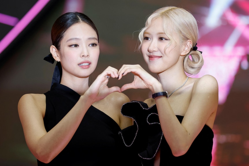 Jennie and Rose smile while holding their hands together in a heart-shape.
