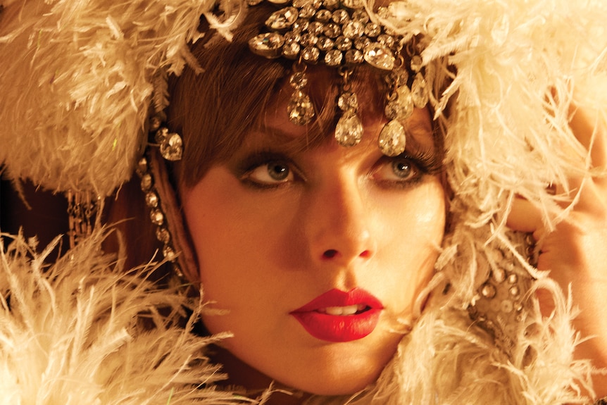 A headshot of Taylor Swift with jewels and feathers surrounding her head.