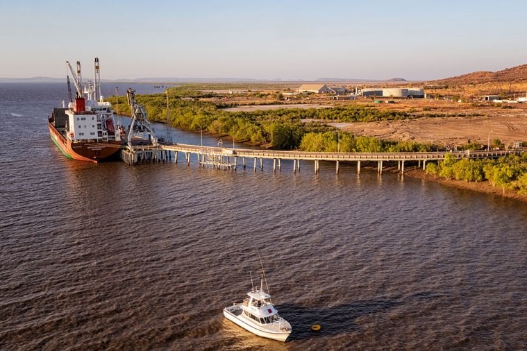 A nickel cargo ship moored at a jetty off a flat coastline.