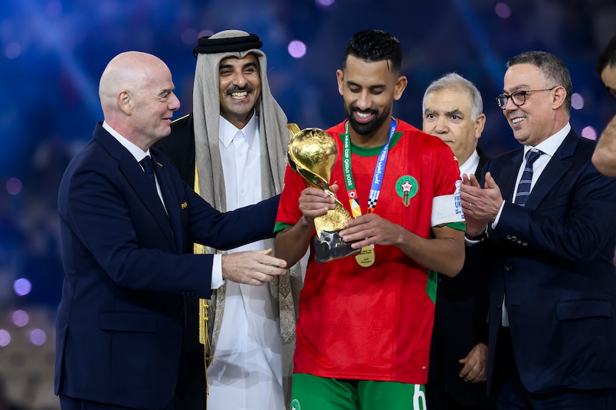 Gianni Infantino presents a trophy to a soccer player, surrounded by other officials