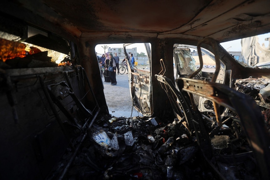 A group of people standing near a destroyed car, looking on, seen from the interior of the vehicle
