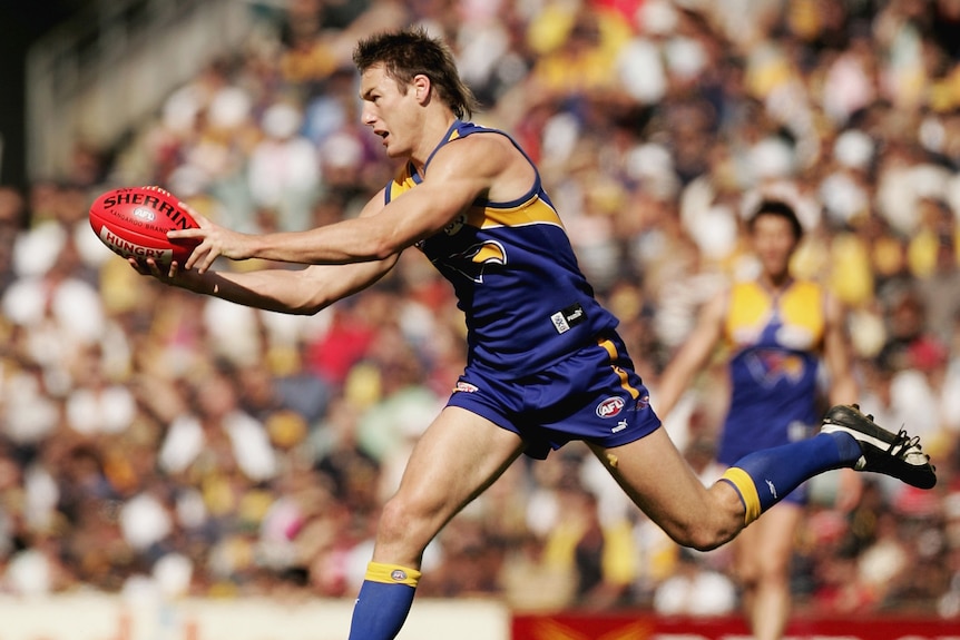 Adam Hunter playing for West Coast. He is mid-run and his arms are outstretched holding the red ball.