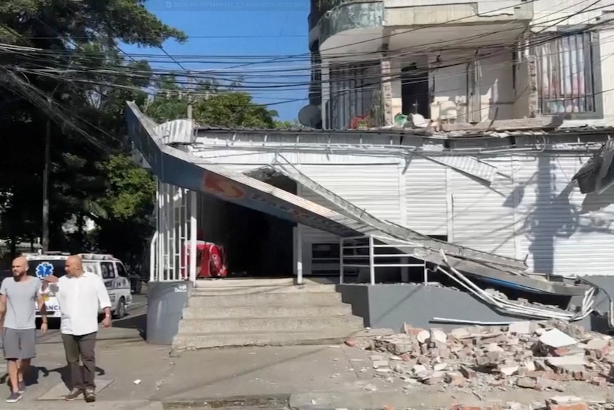 A partially collapsed building seen from the street, with bricks fallen on the ground in front and a collapsed awning.
