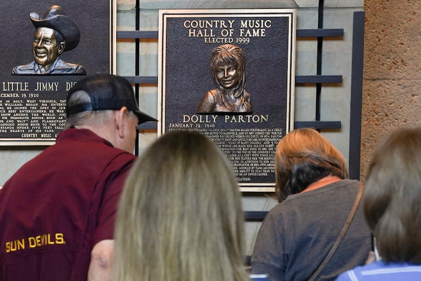 A group gather around a plaque with Dolly Parton on it in the country hall of fame.