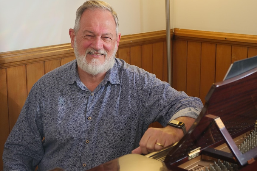 An older, bearded man sits at a piano, beaming.