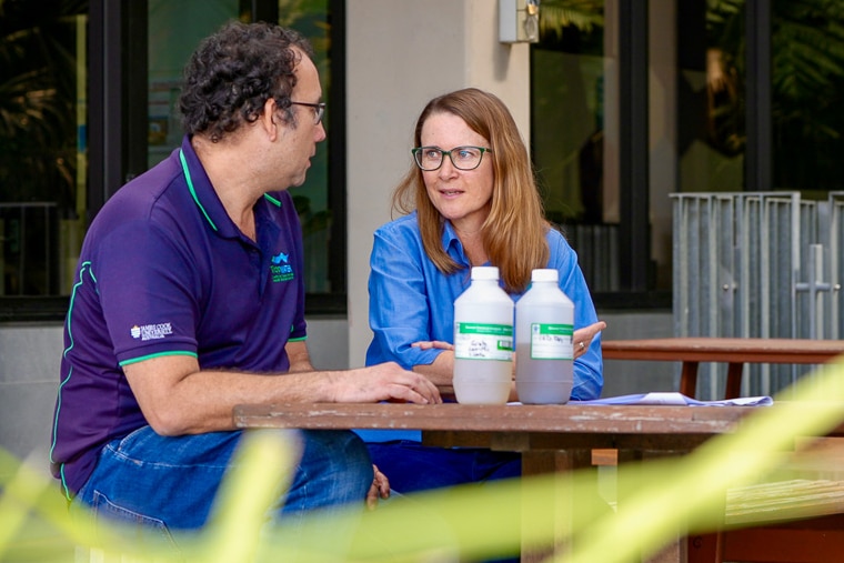 A woman and man in blue shirts talking while sitting at table with water samples
