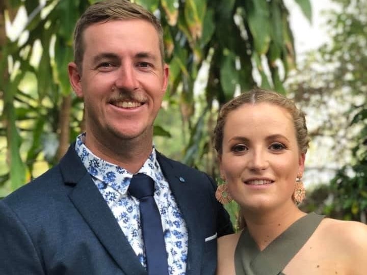 Man with short dark blonde hair and navy suit and woman with dark blonde hair in bun in green dress smiling