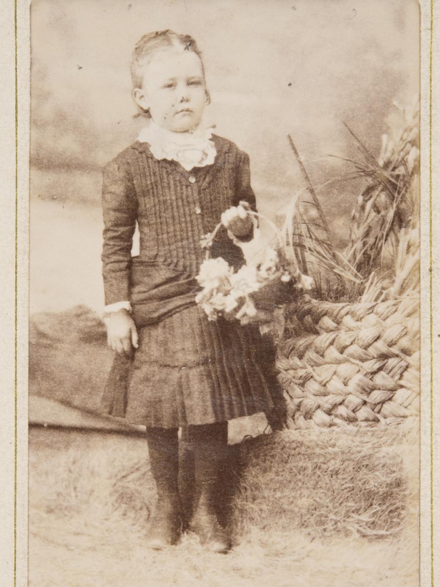 A black and white sepia-toned image of a six-year-old girl holding flowers.