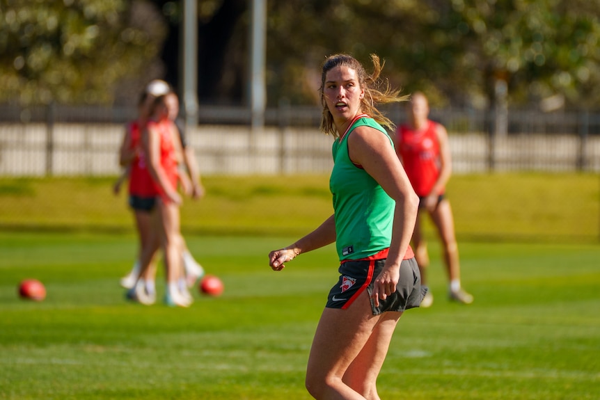 Woman with a green jersey in a field playing aussie rules