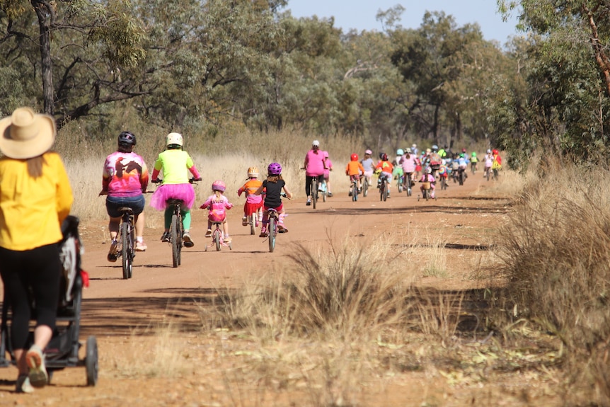 Kids and adults dressed in bright colours riding bikes and walking along a road in the outback.
