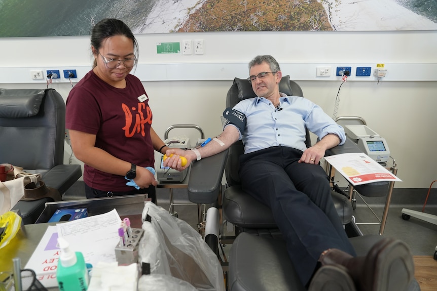 Dr Richard Mitchell lies on a bed at a blood donor centre as a nurse prepares needles