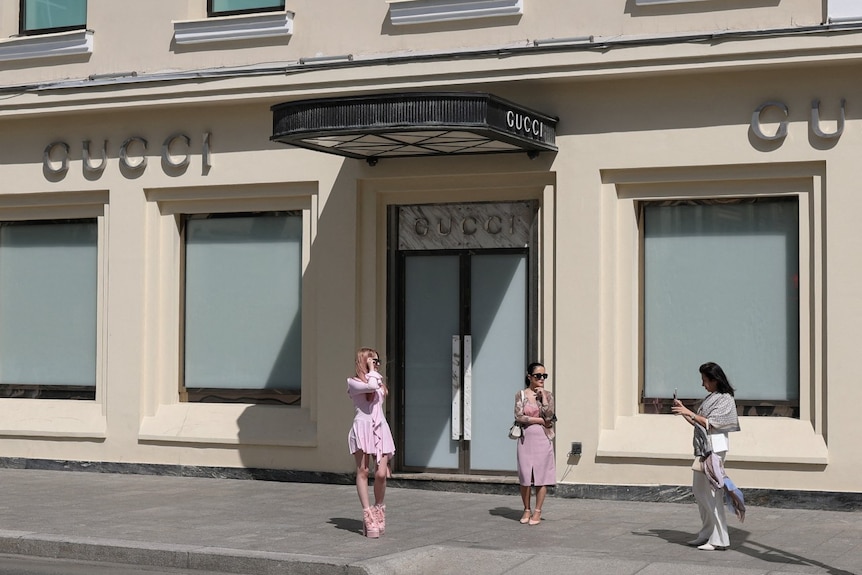 A woman taking pictures of two other women in front of a building that says Gucci on it.