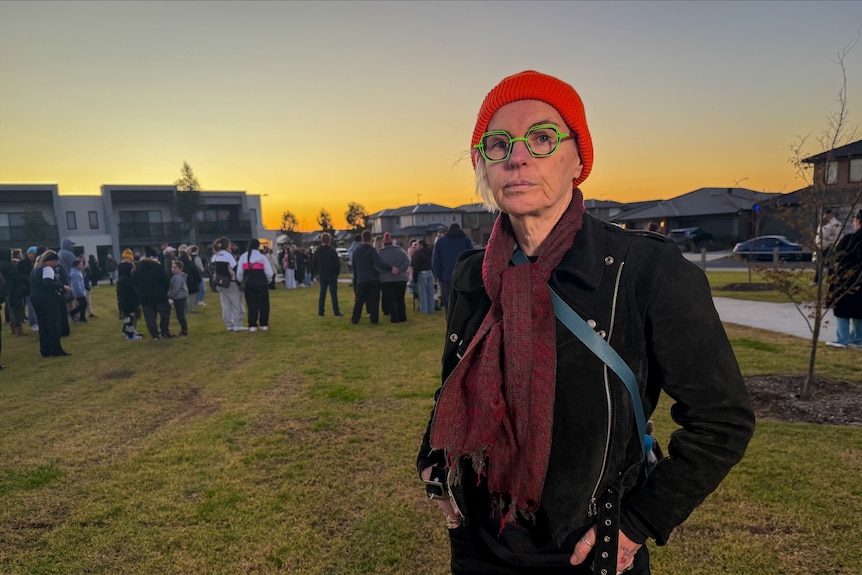 A woman wearing a red beanie and green glasses stands in an open space