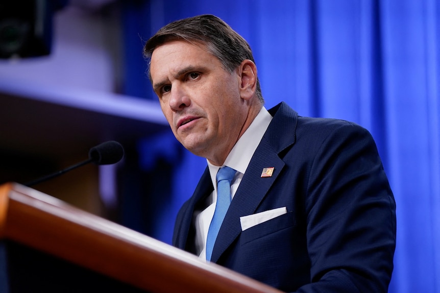 A man with a heavy brow stands at a podium