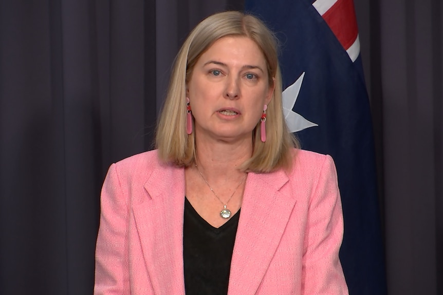 A woman with blonde bobbed hair stands in front of An Australian flag