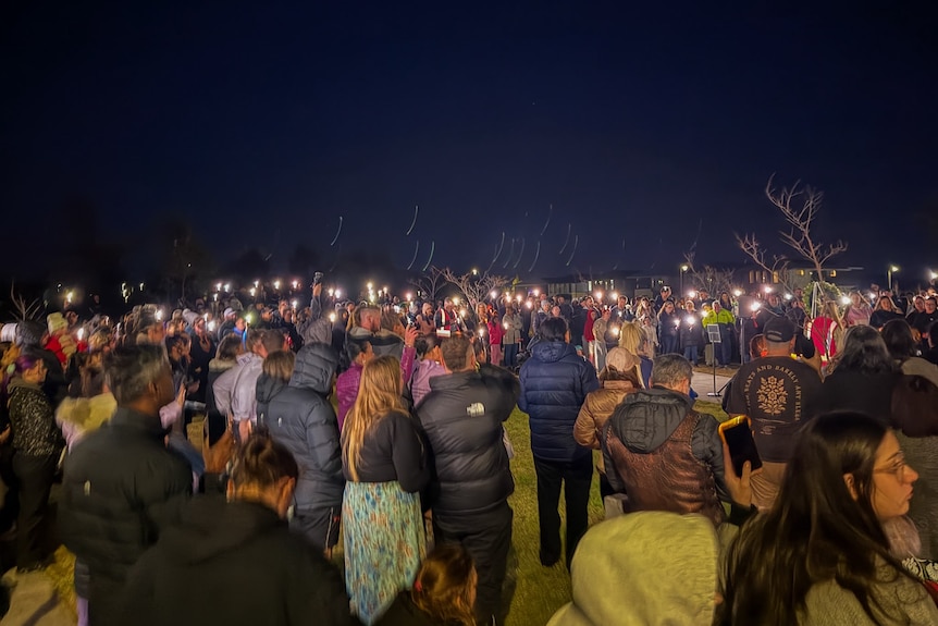 A large group of people stand in an open space holding a vigil for Brooke Stephens