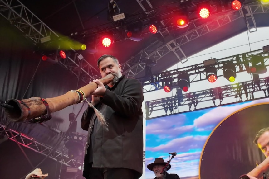 A man plays a didgeridoo on a concert stage