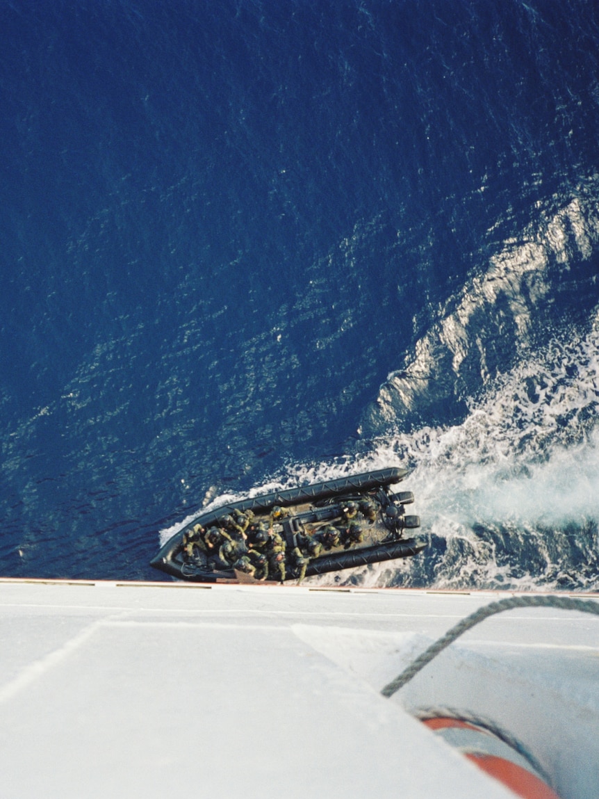 An inflatable military vessel draws close to the side of a large freighter.