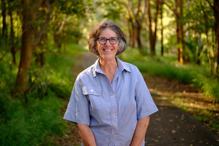 a woman standing near trees smiling at the camera