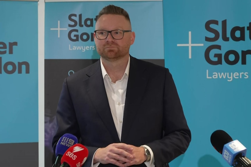 A man in a suit standing in front of Slater and Gordon signage.