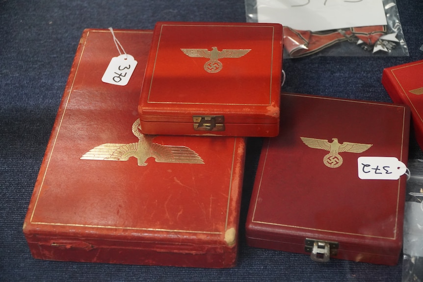 Red boxes of various sizes with gold Nazi-era eagles emblazoned on the lids are on display on a black table.