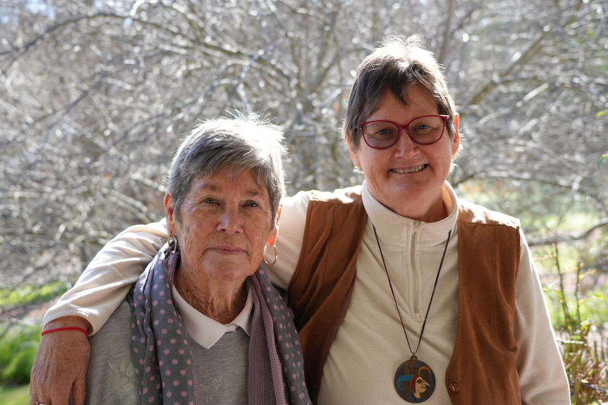 Two older women smiling at the camera outdoors