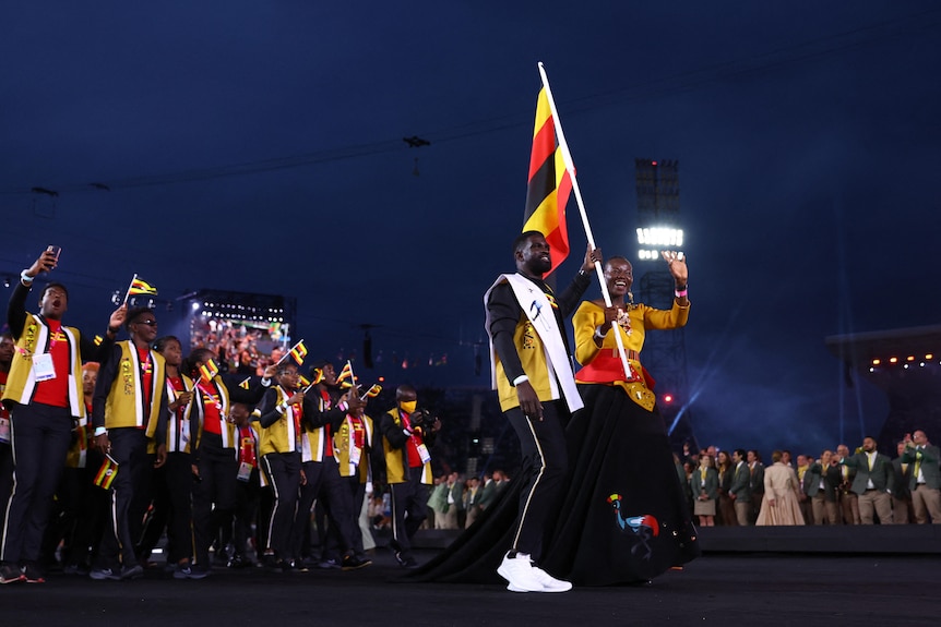 A group of people holding a red, yellow, black striped flag walking through a stadium