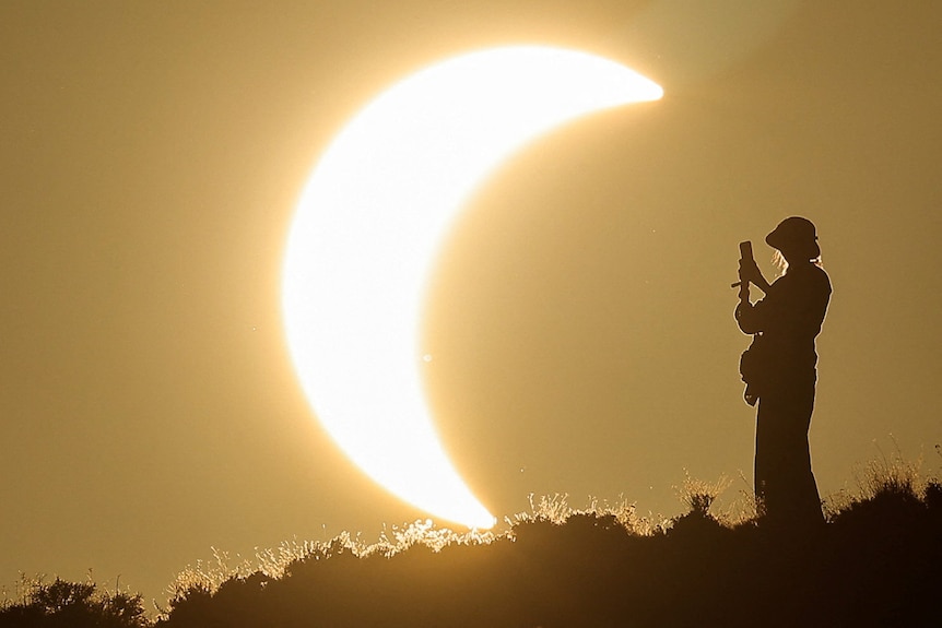 A person takes a photo of a partial solar eclipse.