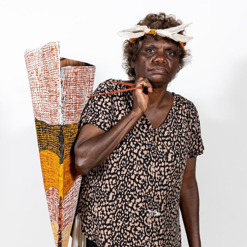 An Indigenous woman wearing a traditional headband that features feathers, holding the bark bag she made and painted.