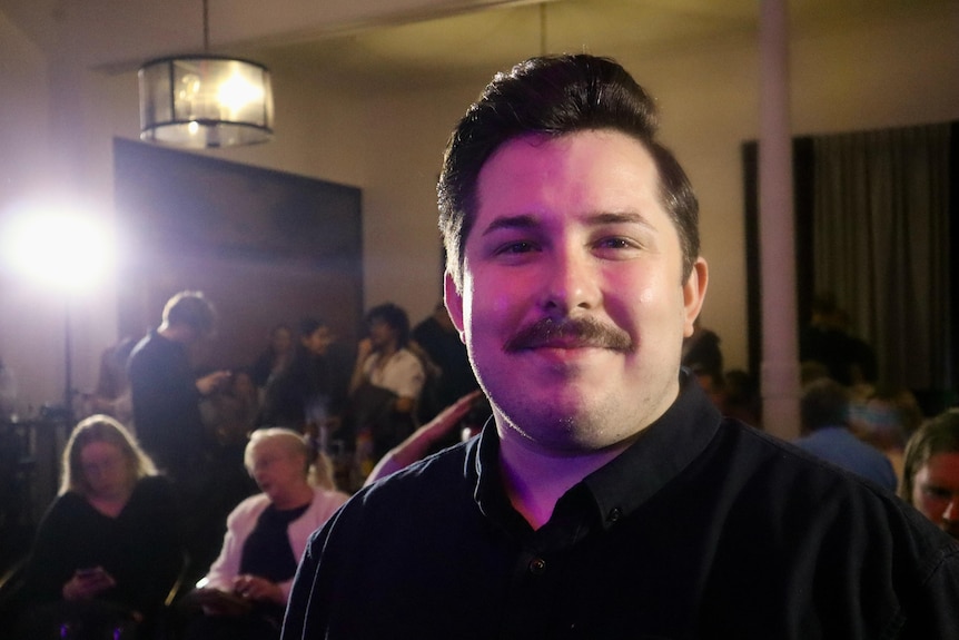 A portrait of a man in a theatre with a crowd of people in the background.
