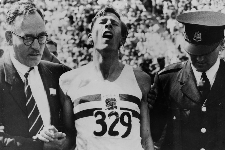 An exhausted Roger Bannister is flanked by two men after the mile final at the 1954 Empire Games.