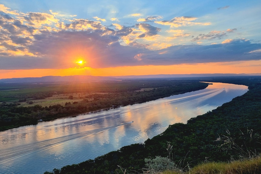 The sky glows orange over a river in a rural setting