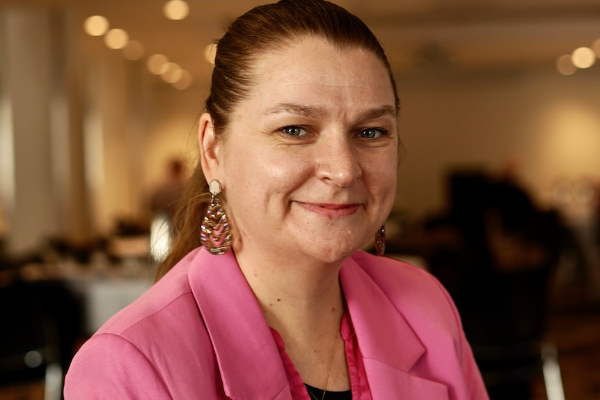 A woman in a pink jacket smiles.