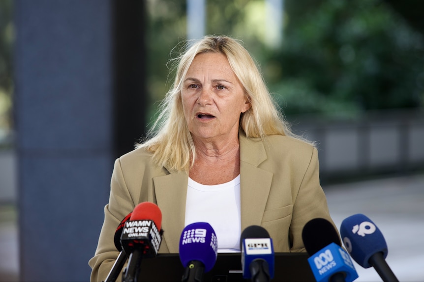 WA Education Minister Sabine Winton speaking into a bunch of microphones outside wearing a beige jacket and white top.