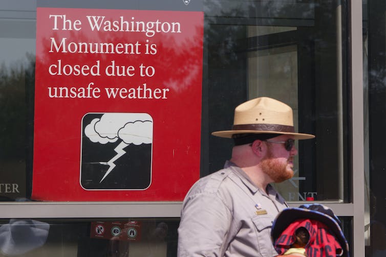 A ranger stands under a sign reading: The Washington Monument is closed due to unsafe weather.